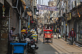 New Delhi, India - 24 June 2025: View of a bustling street scene with rickshaws and people amidst a maze of overhead wires, reflecting the vibrant, chaotic energy of the city.