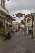 Limassol, Cyprus - 25 June 2025: View of a quiet street scene with a motorcycle parked beneath an ornate sign, brick pavement under a cloudy sky.