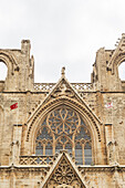 View of the crumbling facade of a historic building adorned with flags, its intricate stonework etched by time under a soft sky, Varosha, Famagusta, Cyprus.