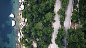 Luftaufnahme der zerklüfteten Küstenlinie, die die Adria küsst, ein üppiger Wald trifft auf eine kurvenreiche Straße, Split, Gespanschaft Split-Dalmatien, Kroatien.