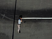 Aerial view of a person standing on a dark asphalt surface, with a white line cutting through the dark expanse, creating a stark contrast in tones, Alessandria, Italy.