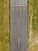 Aerial view of a stark runway stretching out, marked with bright white and yellow lines against the textured asphalt, Tempelhofer Feld, Berlin, Germany.