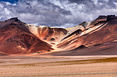 Blick auf zerklüftete Berge, die Schatten auf eine weite, trostlose Ebene unter einem dramatischen Himmel werfen, der die raue Schönheit der Natur zeigt, Departement Potosi, Bolivien.