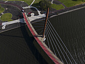 Aerial view of a striking bridge with red accents over the dark water, contrasting with the bright green parkland, creating a vibrant scene, Perth, Western Australia, Australia.