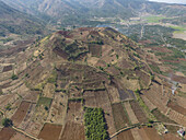Luftaufnahme eines terrassierten Berges mit kontrastreichen Braun- und Grüntönen, umgeben von einem Flickenteppich landwirtschaftlicher Felder, Chu Pah, Gia Lai, Vietnam.