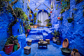 View of a mesmerizing blue-washed alleyway adorned with vibrant potted plants and rustic decor, inviting exploration into its depths, Chefchaouen, Tangier-Tétouan-Al Hoceima, Morocco.