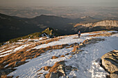 Aerial view of a lone figure standing atop a snow-dusted peak overlooking the distant town nestled amidst rolling hills, Zakopane, Województwo malopolskie, Poland.
