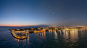 Aerial view of the old city, harbor lights shimmering on the dark waters contrasting with the soft glow of dawn, Acre, North District, Israel.