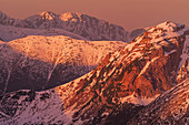 Luftaufnahme der schneebedeckten Berggipfel, die in den warmen Farben der untergehenden Sonne leuchten und einen dramatischen Kontrast zu den kühlen Schatten bilden, Bialka Tatrzanska, Województwo malopolskie, Polen.