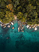 Luftaufnahme des türkisfarbenen Wassers, das auf die felsige Küste und den üppigen grünen Wald trifft, ein tropisches Paradies von oben, Silhouette, La Digue, Seychellen.