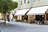 Berlin, Germany - 27 August 2019: View of the quiet cobblestone street lined with charming cafes and shops beneath the soft glow of the awnings.