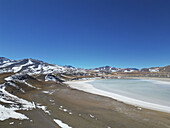 Aerial view of a striking contrast between the stark, snow-dusted mountains and the pale, shimmering lake, a landscape of serene beauty, San Pedro de Atacama, Antofagasta, Chile.