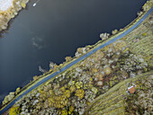 Aerial view of the serene river reflects the sky, bordered by a narrow road and autumnal trees, with a small structure nestled amidst the landscape, Lugo, Lugo, Spain.
