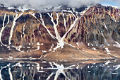 Majestätisch erheben sich schroffe, schneebedeckte Berge, deren Hänge in erdigen Braun- und leuchtenden Rottönen gehalten sind und sich in den ruhigen Gewässern Spitzbergens und Jan Mayens spiegeln.
