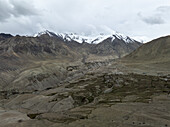 Aerial view of a rugged landscape where the earth meets the sky, capturing the stark beauty of snow-capped peaks against a vast, arid terrain, Leh, Ladakh, India.