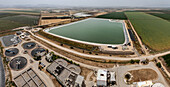 Luftaufnahme einer Kläranlage im Kontrast zu den geometrischen grünen Feldern dahinter, die eine Mischung aus Industrie und Landwirtschaft widerspiegeln, Kfar Masaryk, North District, Israel.