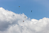 Blick auf farbenfrohe Gleitschirmflieger, die inmitten der flauschigen weißen Wolken unter einem weiten blauen Himmel tanzen und ein Gefühl von Freiheit und Abenteuer vermitteln, Oderen, Grand Est, Frankreich.