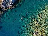 Aerial view of a swimmer adrift in the turquoise waters near the rocky coast, a serene dance between nature's palette and human presence, Kaloi Limenes, Heraklion, Greece.