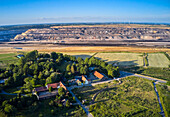 Luftaufnahme einer riesigen Braunkohlegrube im Kontrast zu den grünen Feldern und verstreuten landwirtschaftlichen Gebäuden, ein Nebeneinander von Industrie und Natur, Lutzerath, Rheinland-Pfalz, Deutschland.