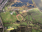 Aerial view of green sports fields, a running track, and a winding stream nestled beside a series of lakes, creating a tapestry of nature and recreation, Barn Elms Playing Field, Rocks Lane recreation ground, water reservoir lagoon at river Thames London, United Kingdom.