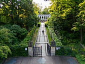 Luftaufnahme einer einsamen Gestalt, die den terrassenförmigen Weg zur Kolonnade hinaufsteigt, eingerahmt von üppigem Grün, eine ruhige Szene in Friedrichshain-Kreuzberg, Berlin, Volkspark Friedrichshain, Deutschland.