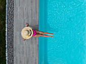 Aerial view of a woman sunbathing in a pink swimsuit and straw hat next to a blue swimming pool, Strasbourg, Grand Est, France.