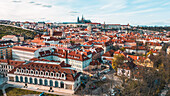 Aerial view of terracotta rooftops cascading towards the majestic Prague Castle under a serene sky, a timeless tableau of history and beauty, Prague, Czechia.