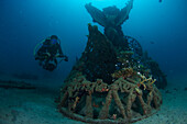 Der Blick auf eine Unterwasserszene zeigt einen Taucher, der eine unter Wasser liegende Struktur erkundet, die mit Meerespflanzen bewachsen ist, was einen heiteren Kontrast schafft, Pemuteran, Bali, Indonesien.