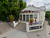 Berlin, Germany - 30 May 2025: Aerial view of the Theater am Friedrichshain, its white facade glowing softly against the lush green backdrop of trees.