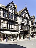 Dartmouth, United Kingdom - 05 October 2025: View of timber-framed buildings casting shadows on the street, their dark wooden beams contrasting with the bright sky and the bustle of daily life..