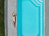 Aerial view of a woman in a swimsuit basking in the sun next to the turquoise pool, a geometric oasis of leisure, Strasbourg, Grand Est, France.
