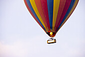 View of a vibrant hot air balloon with red, yellow, and blue panels soaring through the serene sky with flames ignited below, Narok, Narok, Kenya.