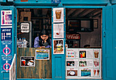 Dhangadhi, Nepal - 03. März 2023: Blick auf eine Frau in einem kleinen Laden mit hellblau gestrichenen Türen und Fensterrahmen, die kalte Getränke und Tee anbietet, ein Einblick in den lokalen Handel.