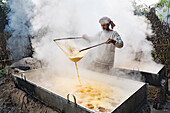 Natore, Bangladesh - 17 January 2023: View of a man straining liquid from a vat amidst billows of white steam, creating a scene of labor and tradition.