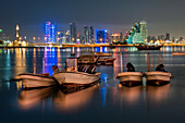 Manama, Bahrain - 29 May 2022: View of boats bobbing gently on the water, reflecting the bright, colorful lights of the Manama skyline at night.