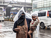 Chittagong, Bangladesch - 06. August 2023: Blick auf eine Mutter, die ihr Kind vor dem Regen in der Nähe des GEC Circle schützt. Der Regen spiegelt die düstere Stimmung in der Stadt wider.