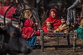 Kolkata, India - 28 January 2023: View of a vibrant scene unfolds with women and children in red attire, seated on a charpai, amidst the rustic charm.