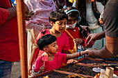 Bogura, Bangladesh - 03 November 2023: View of children's faces lit with curiosity as they reach for treats at a vibrant street vendor stall, a scene filled with the warmth of human connection.