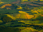 Aerial view of rolling green hills and fields create a textured landscape, with shadows and sunlight painting a picturesque scene, Sete Cidades, Portugal.