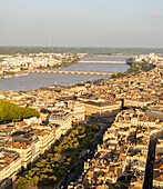 Luftaufnahme des Flusses Garonne, der durch einen Teppich aus Terrakotta-Dächern und sonnenbeschienenen Fassaden fließt, ein lebendiges Stadtbild, Bordeaux, Frankreich.