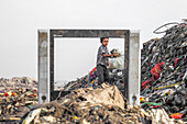 Chittagong, Bangladesh - 15 November 2018: View of a young boy amidst a sprawling landfill, framed by a discarded television set, a poignant contrast of innocence and desolation.
