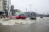 Chattogram, Bangladesh - 05 August 2023: View of a flooded street scene where a red car battles through the muddy deluge near local transportation.