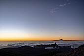 Blick auf eine ruhige Landschaft, in der der Horizont in einem Spektrum von Farben leuchtet, von feurigem Orange bis zu sanftem Blau, über einem Meer von Wolken, Pico de las Nieves, Kanarische Inseln, Spanien.