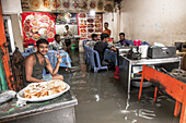 Chattogram, Bangladesh - 05 August 2023: View of customers wading through floodwaters inside a restaurant, a stark contrast to the colorful food displayed on the wall.