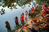 Bogura, Bangladesh - 20 November 2023: View of women in vibrant saris offering prayers in the serene water, surrounded by colorful flowers and fruit-filled baskets.