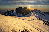 Luftaufnahme der majestätischen, schneebedeckten Berggipfel, die vom goldenen Licht der aufgehenden Sonne geküsst werden und die zerklüftete Landschaft beleuchten, Mount Kenia, Kenia.