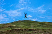 Sunamganj, Bangladesh - 27 January 2019: View of a joyful leap against a vibrant blue sky, above the undulating green hills, a moment frozen in time.