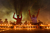 Narayanganj, Bangladesh - 11 June 2018: View of individuals gathered in a low-lit space, hands raised amidst an array of glowing candles, casting a warm, ethereal light.
