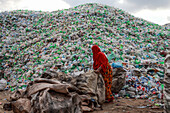Chittagong, Bangladesch - 22. September 2022: Eine Frau in leuchtendem Orange steht inmitten eines riesigen Berges aus weggeworfenen Plastikflaschen, die einen starken Kontrast zum bedeckten Himmel bilden.
