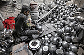 Keraniganj, Bangladesh - 27 December 2020: View of a young boy amidst a sea of gleaming, polished metal pots, diligently working in a dimly lit workshop, surrounded by tools and materials.